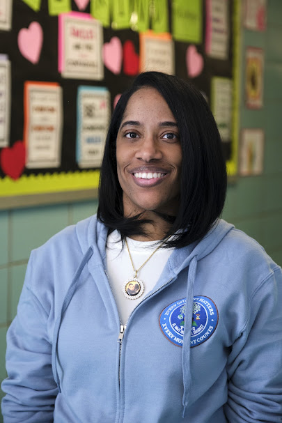 Ms. Banks smiling in classroom wearing school zip-up hoodie