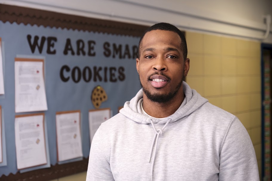 Mr. Primus smiling in front of a school bulletin board