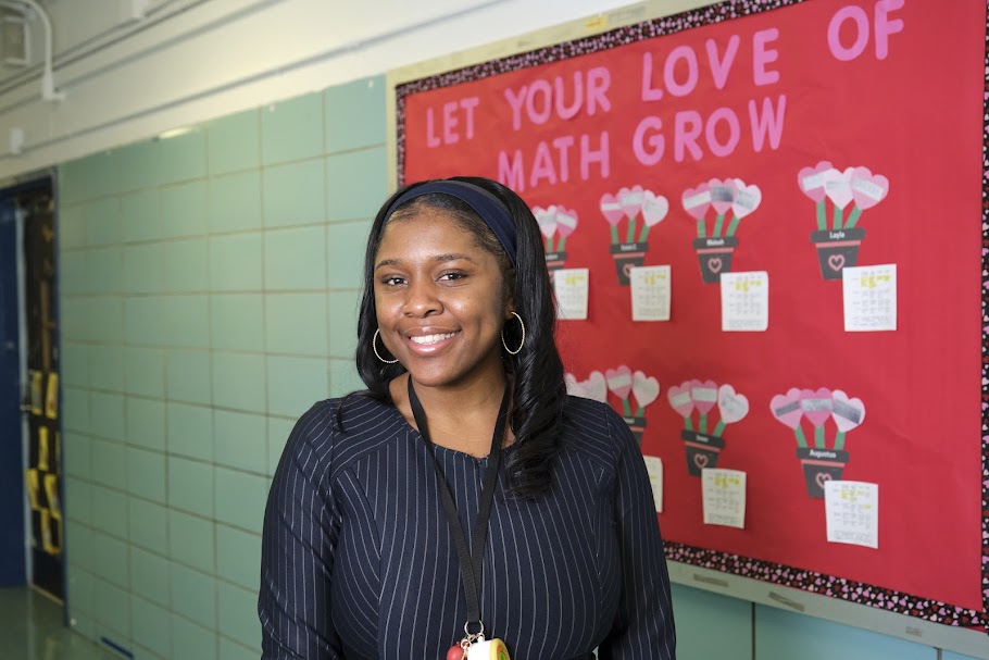 Teacher smiling in front of a math bulletin board display