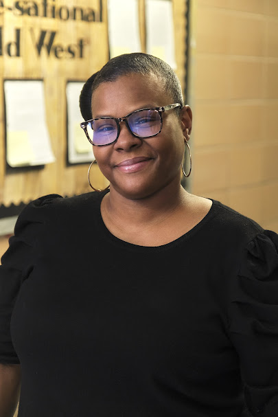 Ms. Foster smiling in front of a classroom bulletin board