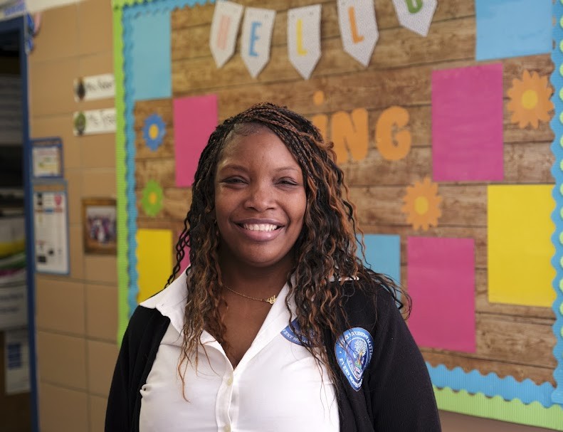 Ms. Setrana smiling in front of a colorful classroom bulletin board