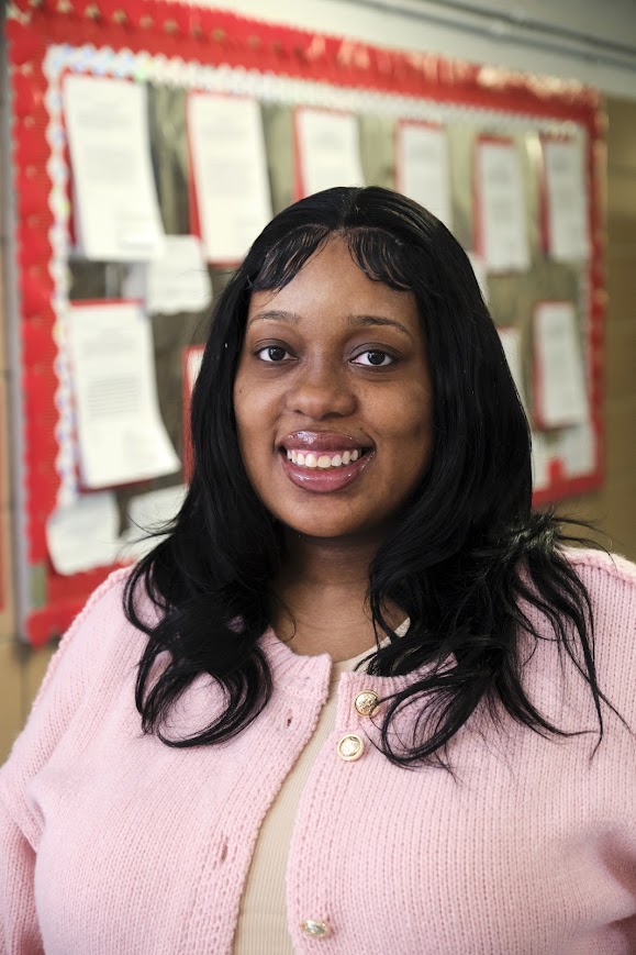 Ms. Rodney smiling in front of a classroom bulletin board