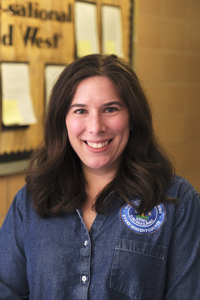 Ms. Roberts smiling in front of a classroom bulletin board
