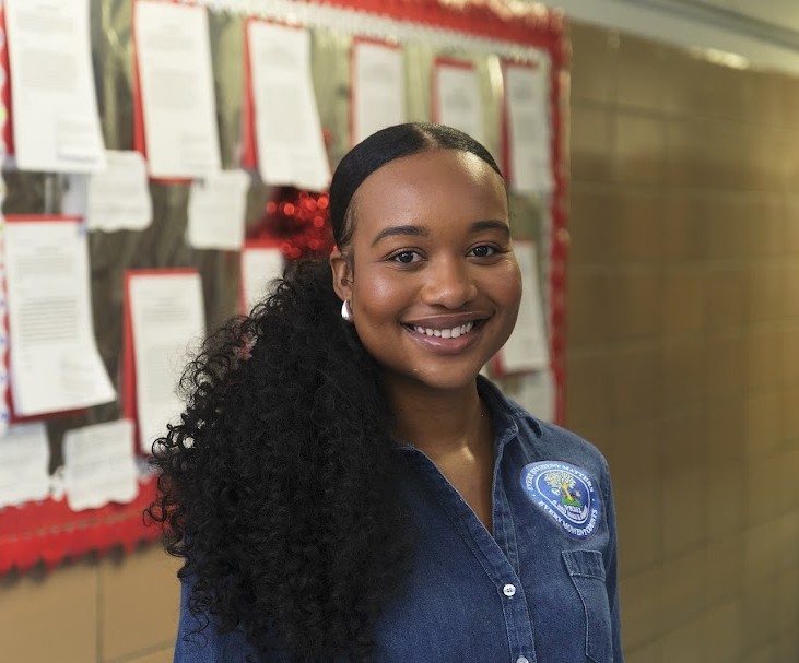 Ms. Cousins smiling in front of a school bulletin board