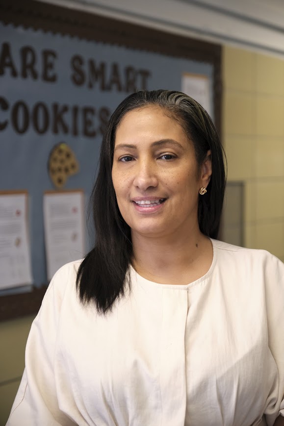 Ms. Hamilton smiling in front of a classroom bulletin board