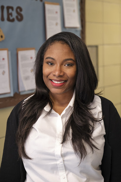 Ms. Lee smiling in front of a classroom bulletin board
