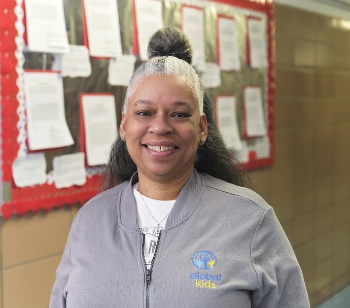 Ms. Jackson-Dilligard smiling in Global Kids jacket near bulletin board