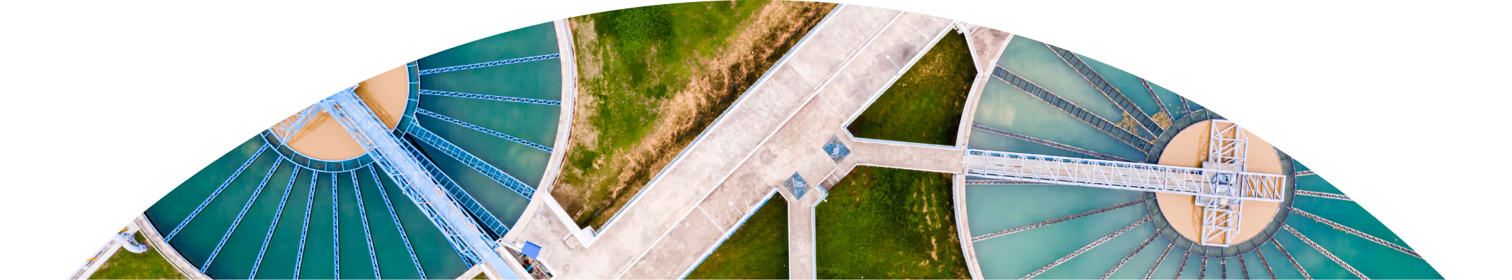 Aerial view of a large circular water treatment plant with multiple green water tanks and connecting walkways.
