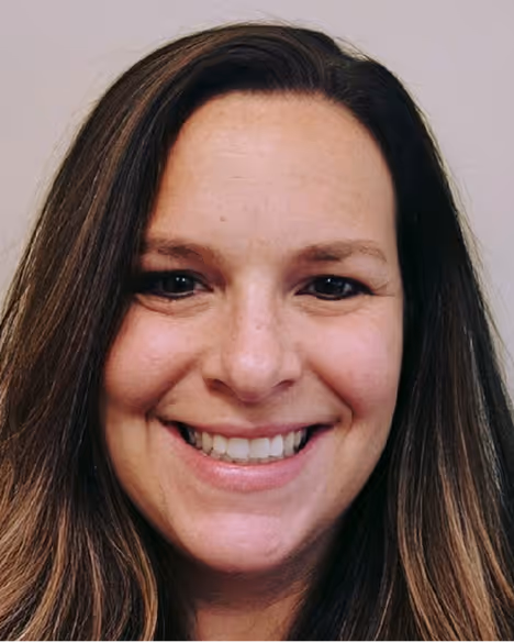 Smiling woman with long brown hair and a light background.