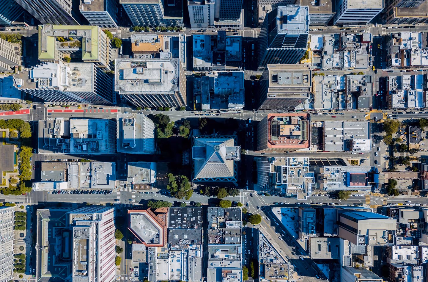 Aerial view of a city block with multiple skyscrapers casting long shadows on streets below.