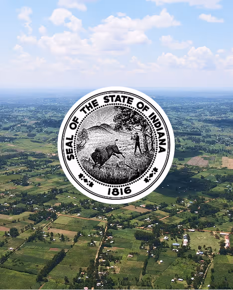 Seal of the State of Indiana featuring a woodsman chopping a tree and a bison, overlaid on an aerial view of green farmland and scattered houses under a partly cloudy sky.
