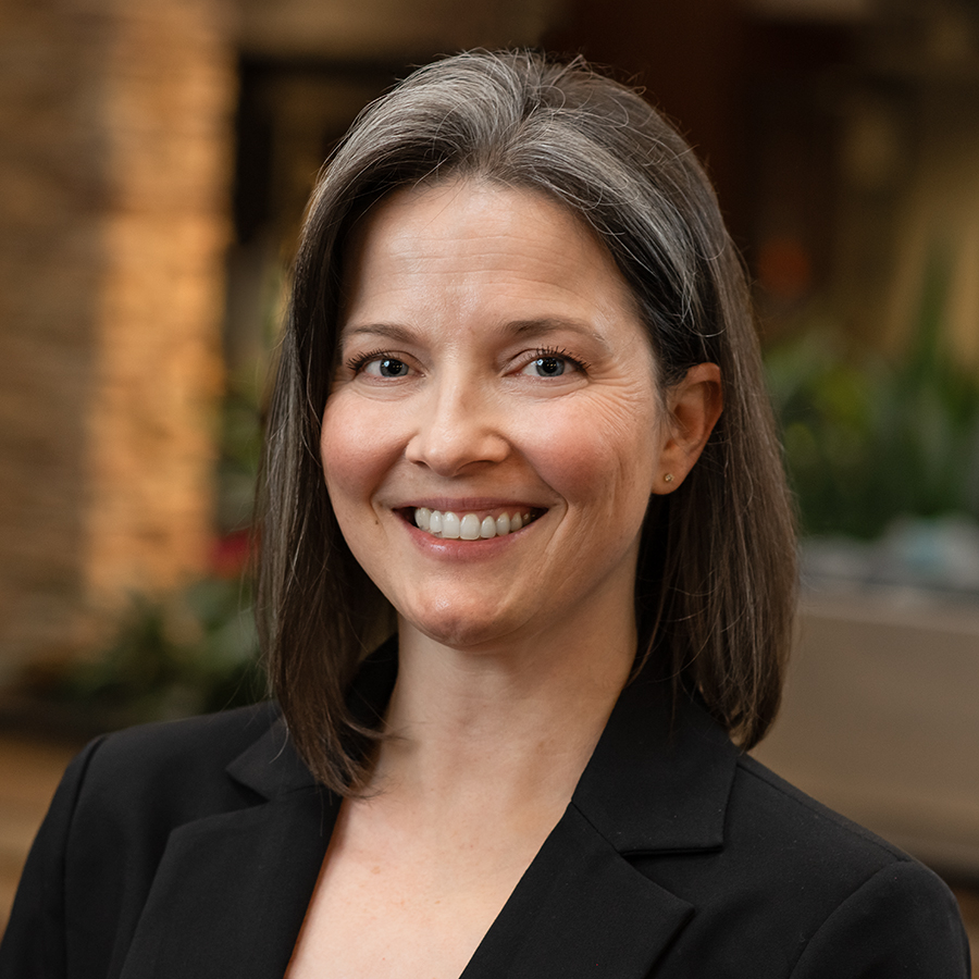 Smiling woman with shoulder-length gray hair wearing a black blazer in an indoor setting.