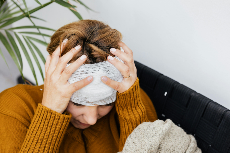 A woman sitting down holds her hands to her bandaged head