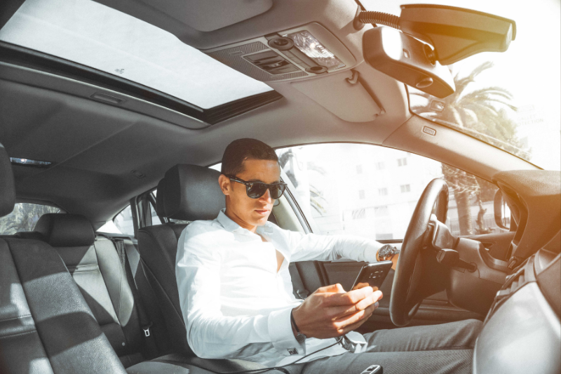 A man in white collared shirt and sunglasses is texting while driving his car