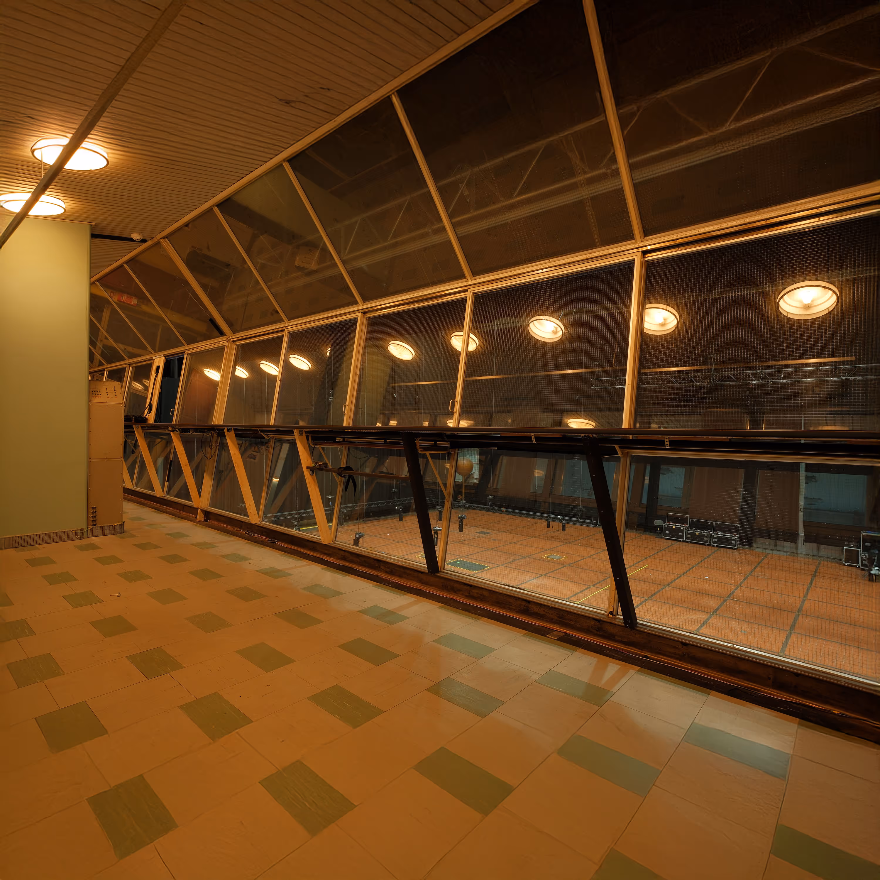 Balcony overlooking an indoor sports court with a tiled floor and ceiling lights.