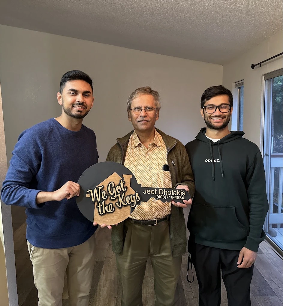 Three men smiling indoors holding a large key-shaped sign saying We Got the Keys, Jeet Dholakia.