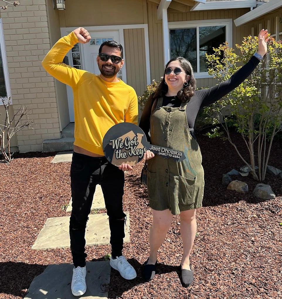 Smiling man and woman standing outside a house holding a sign that says We Got the Keys.
