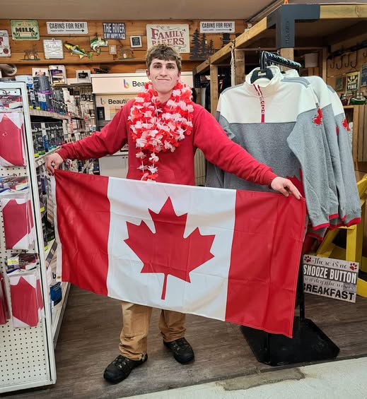 Young man in a store holding a Canadian flag, wearing a red shirt and red-and-white lei.