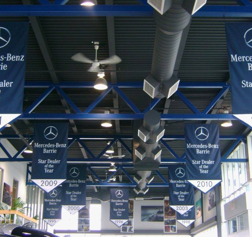 Indoor ceiling of a car dealership with multiple banners displaying Mercedes-Benz Barrie Star Dealer of the Year awards from various years.