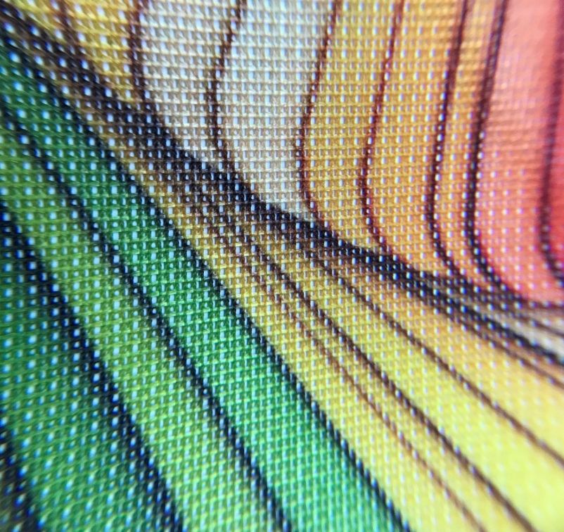 Close-up of a colorful printed fabric showing the texture of woven threads with green, yellow, and orange stripes.
