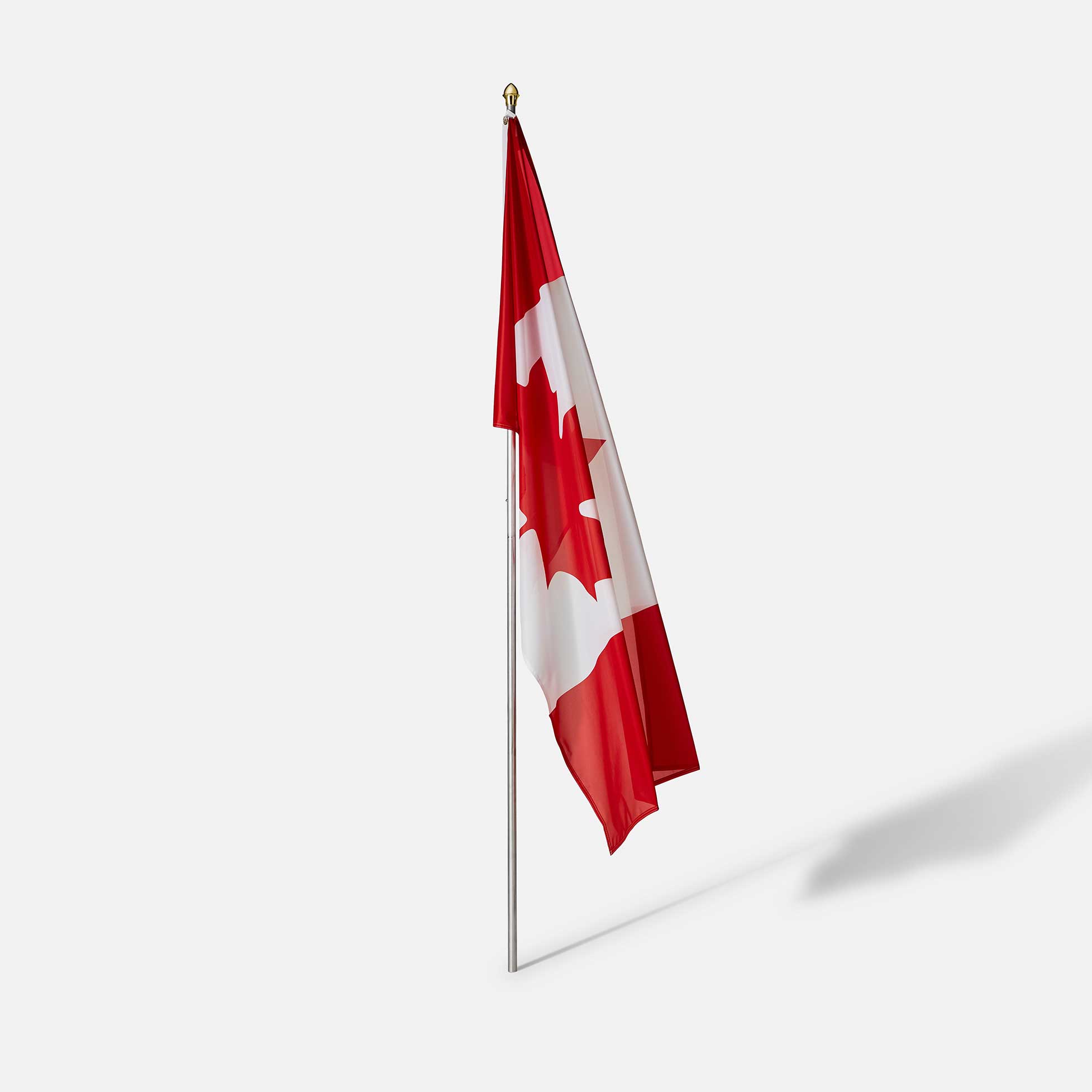 Canadian flag hanging vertically on an indoor metal flagpole casting a shadow on a light background.