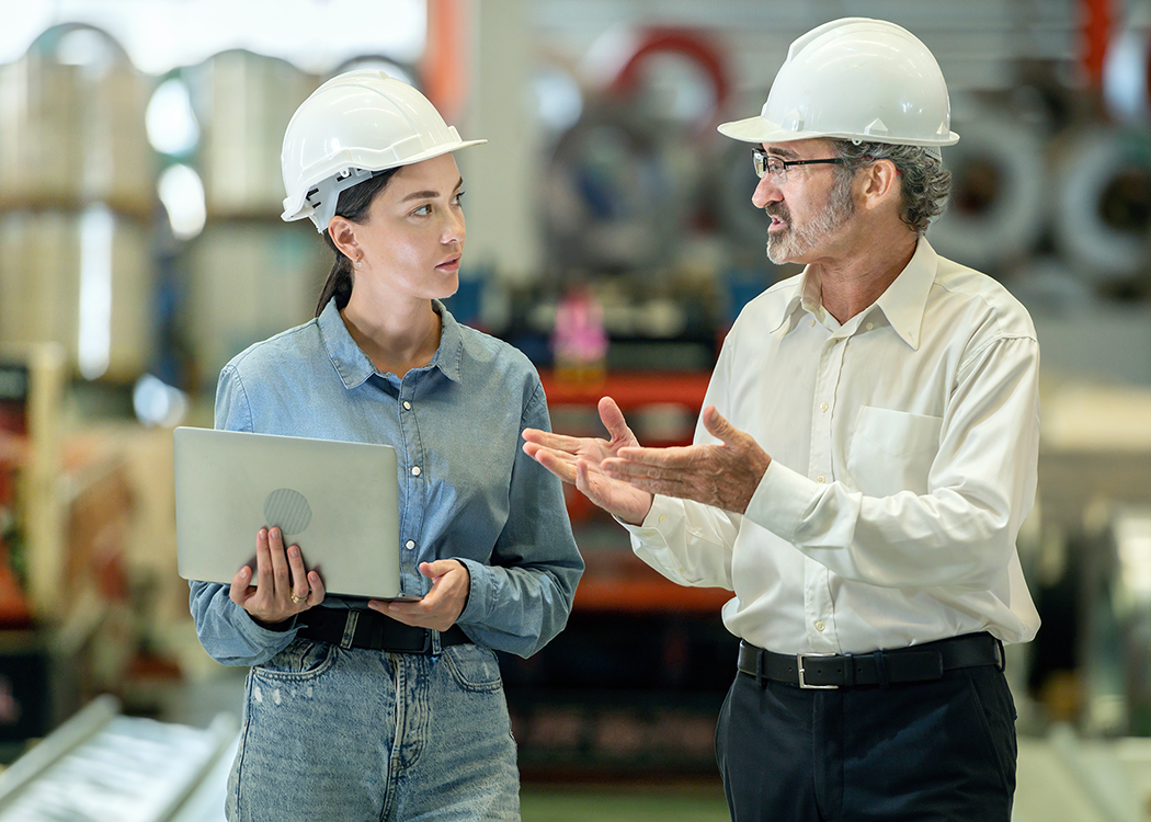 Deux professionnels portant des casques de sécurité consultent des documents sur une tablette dans une installation industrielle.