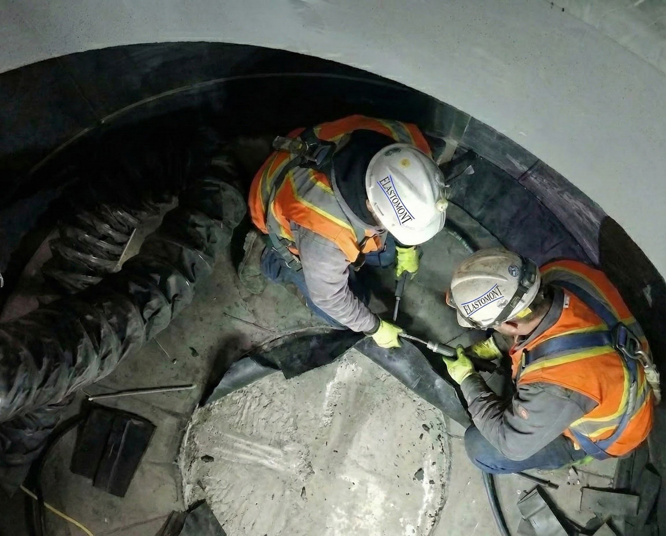 Ouvriers sur un chantier en train de réparer le revêtement en caoutchouc d'un réservoir, portant des casques Elastomont.