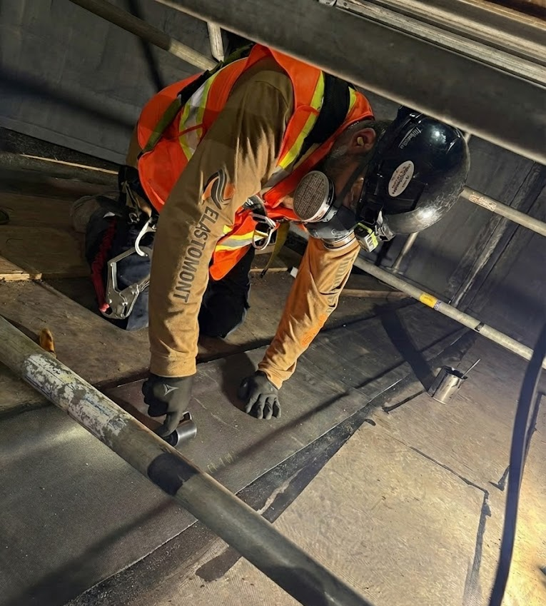 Spécialiste d'Elastomont équipé d'un masque de protection appliquant un revêtement de caoutchouc (rubber lining) à cuite chimique à l'intérieur d'un réservoir d'une usine de lithium.