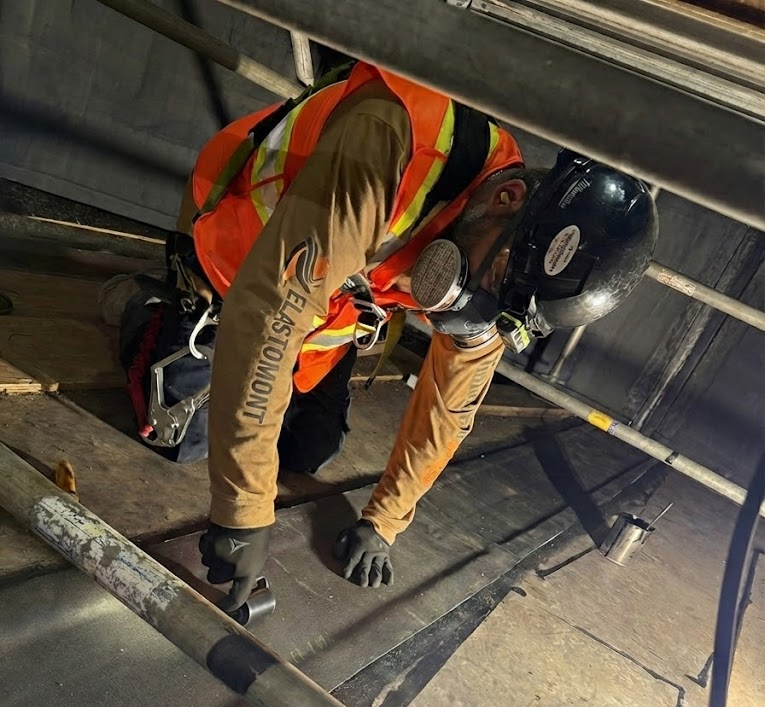 Spécialiste d'Elastomont équipé d'un masque de protection appliquant un revêtement de caoutchouc (rubber lining) à cuite chimique à l'intérieur d'un réservoir d'une usine de lithium.