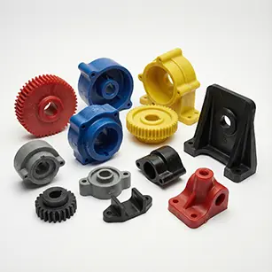 Photo détaillée d'une variété de pièces industrielles moulées en polyuréthane, incluant des engrenages, des boîtiers et des supports, de couleurs rouge, bleu, jaune, noir et gris, disposées sur un fond blanc uniforme.