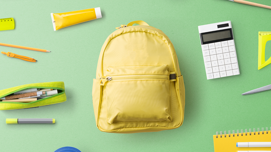Back-to-school supplies, such as a backpack, calculator, pencil case, and pen, laid out on a table.
