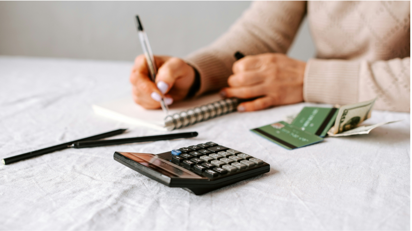 A person using a calculator while reviewing cash, credit cards, and a notebook.