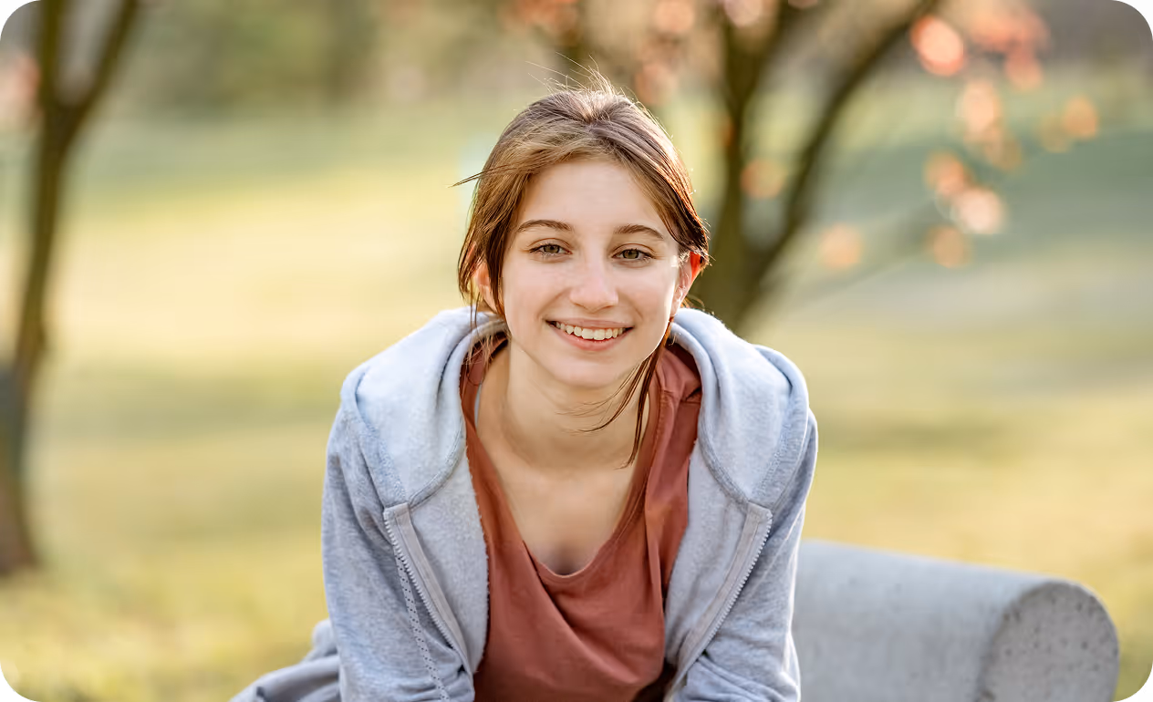 Adolescente sonriente mirando a cámara en un entorno de parque, transmitiendo bienestar y autoestima