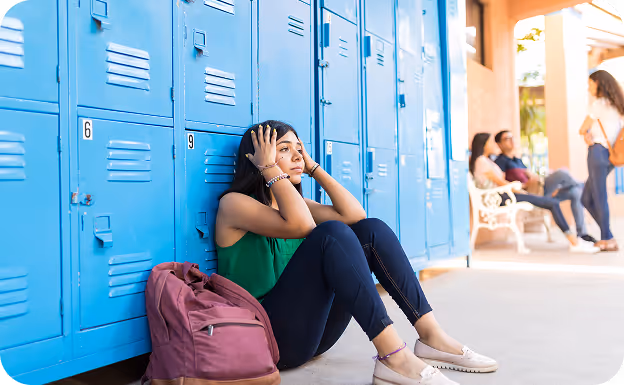 Adolescente sentada en el piso delante de las taquillas de una escuela con cara de desesperanza