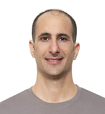 Smiling man with beard and mustache wearing a light gray button-up shirt with arms crossed against a plain gray background.