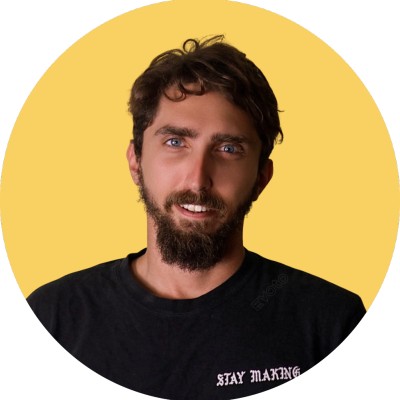 Man with curly hair and a beard wearing a black shirt with 'STAY MAKING' text, smiling against a yellow background.