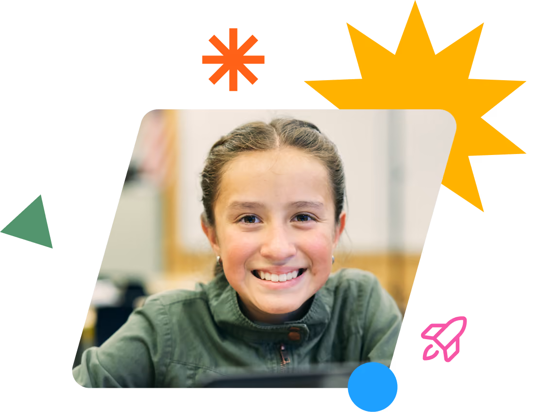 Smiling young girl with braided hair wearing a green jacket in a classroom setting.