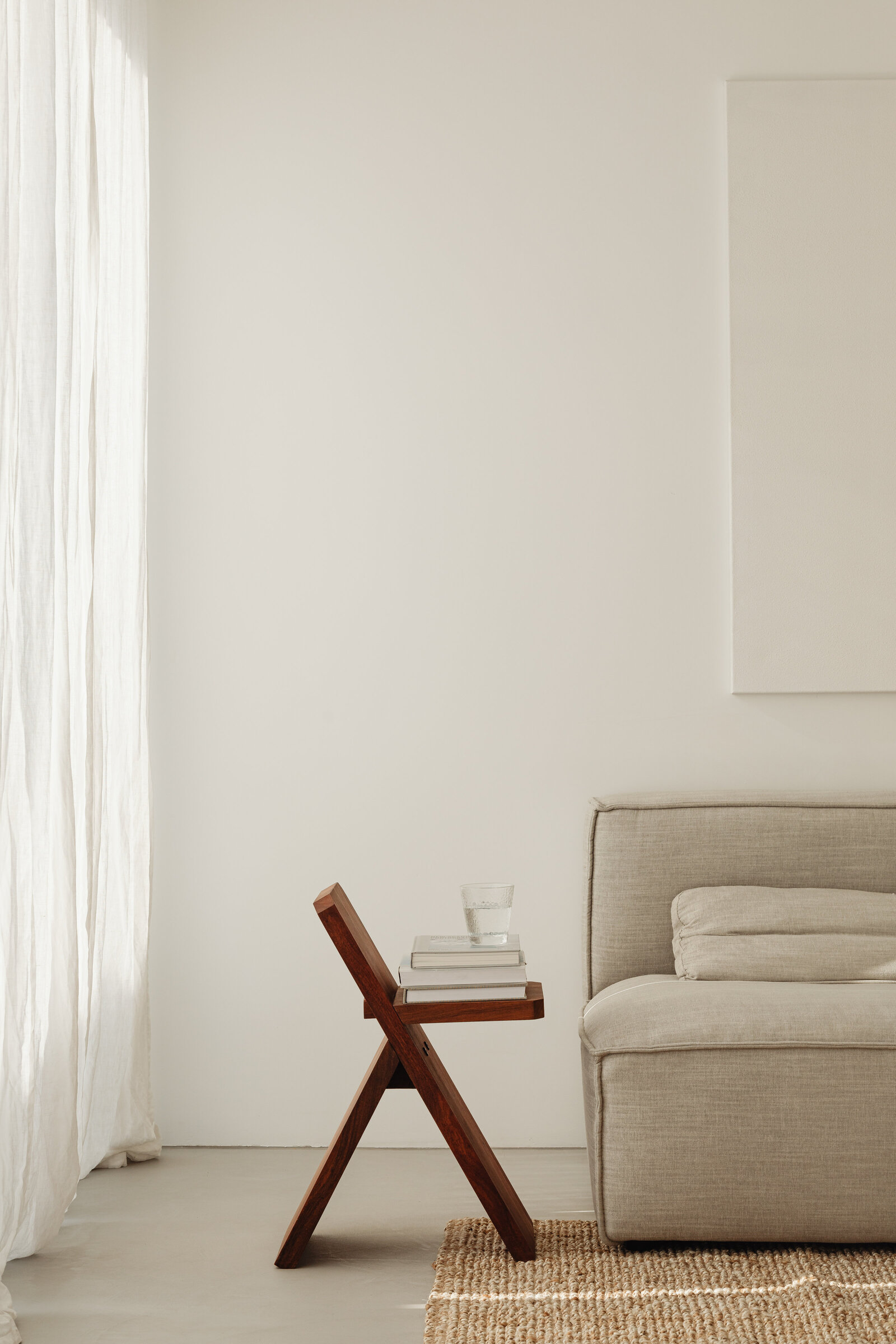 Neutral interior with white curtains, beige sofa and wooden stool