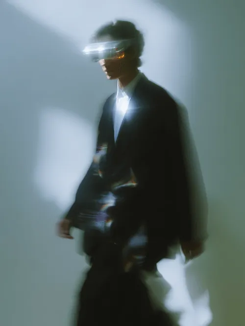 Blurred silhouette of a person wearing futuristic glasses and a suit walking in soft light.