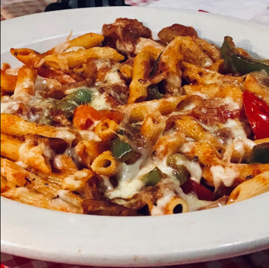 A plate of pasta topped with meat and colorful vegetables, garnished with herbs.