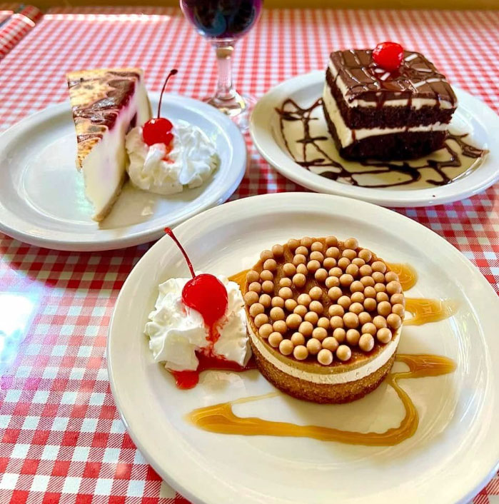 A table set with three plates of various desserts and a bottle of wine.