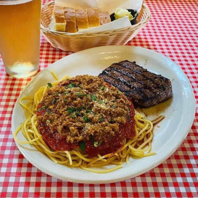 A plate of spaghetti topped with meat sits on a table.