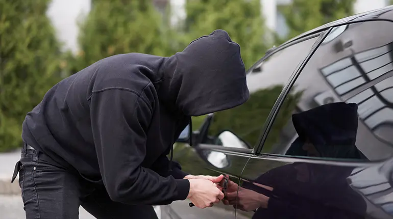 An anonymous individual in a hooded jumper testing the lock on a car in a driveway.