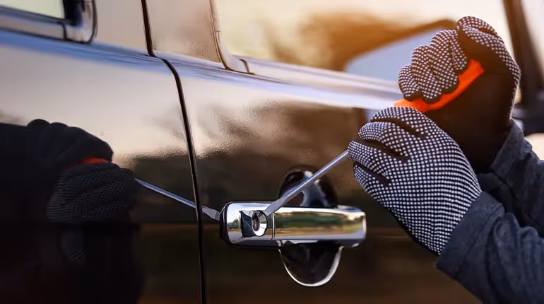 Close-up of a thief’s hands as they use a screwdriver to try and break a car door lock.