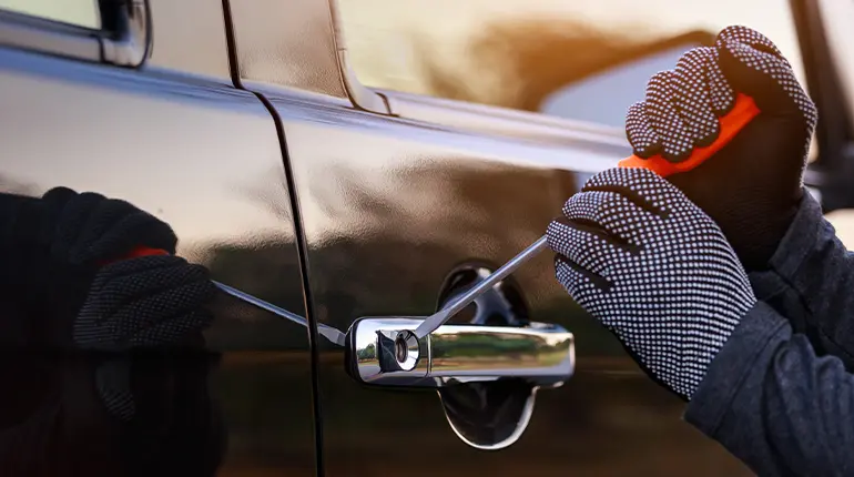 Close-up of a thief’s hands as they use a screwdriver to try and break a car door lock.