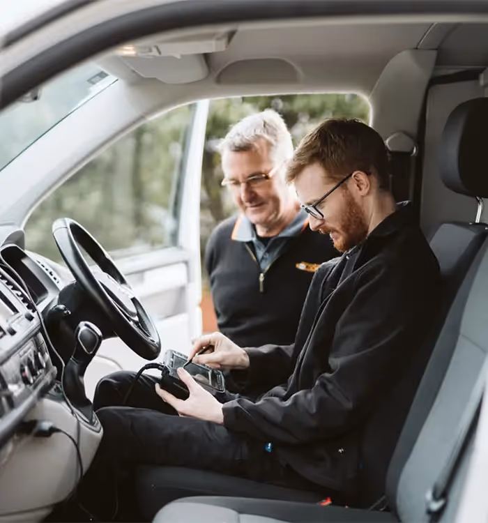 Two men working together in a car, examining a device