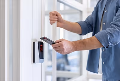 A man using his phone to tap a digital access control lock at his workplace.