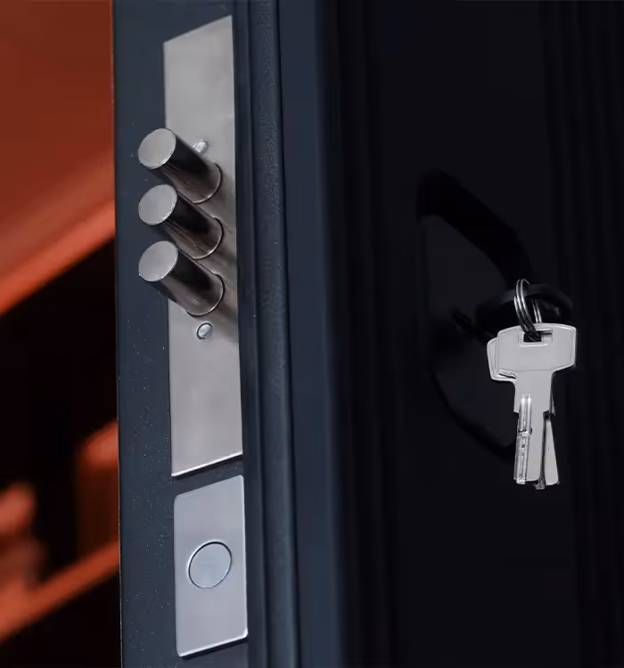 Modern door lock with three bolts and keys hanging on dark background