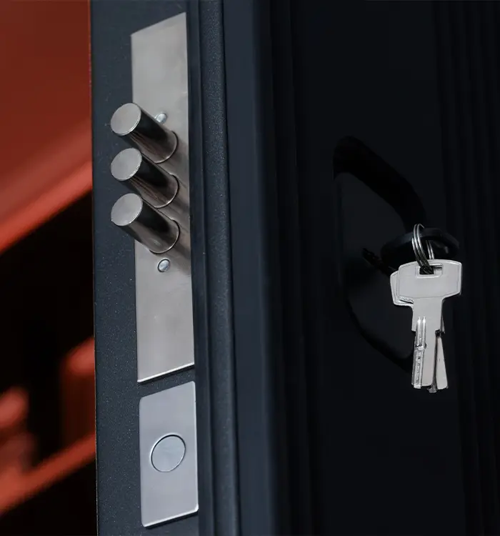 Modern door lock with three bolts and keys hanging on dark background