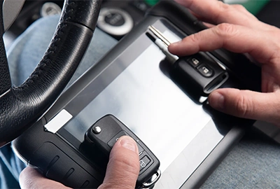A close-up of our locksmith's hands holding a client’s car key, a freshly cut duplicate, and a portable tablet we use to program fobs.